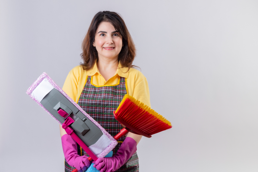 A woman wearing an apron stands with a broom and cleaning supplies, showcasing Kainos Cleaning's pool service in Orlando